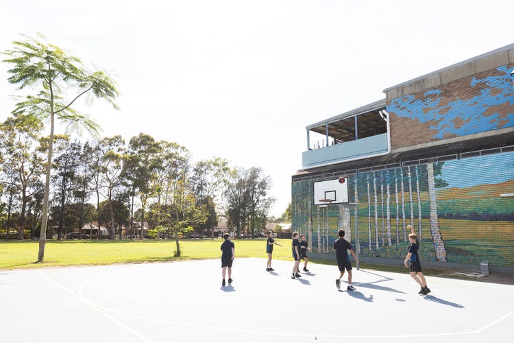A hero banner of students playing basketball next to the oval.